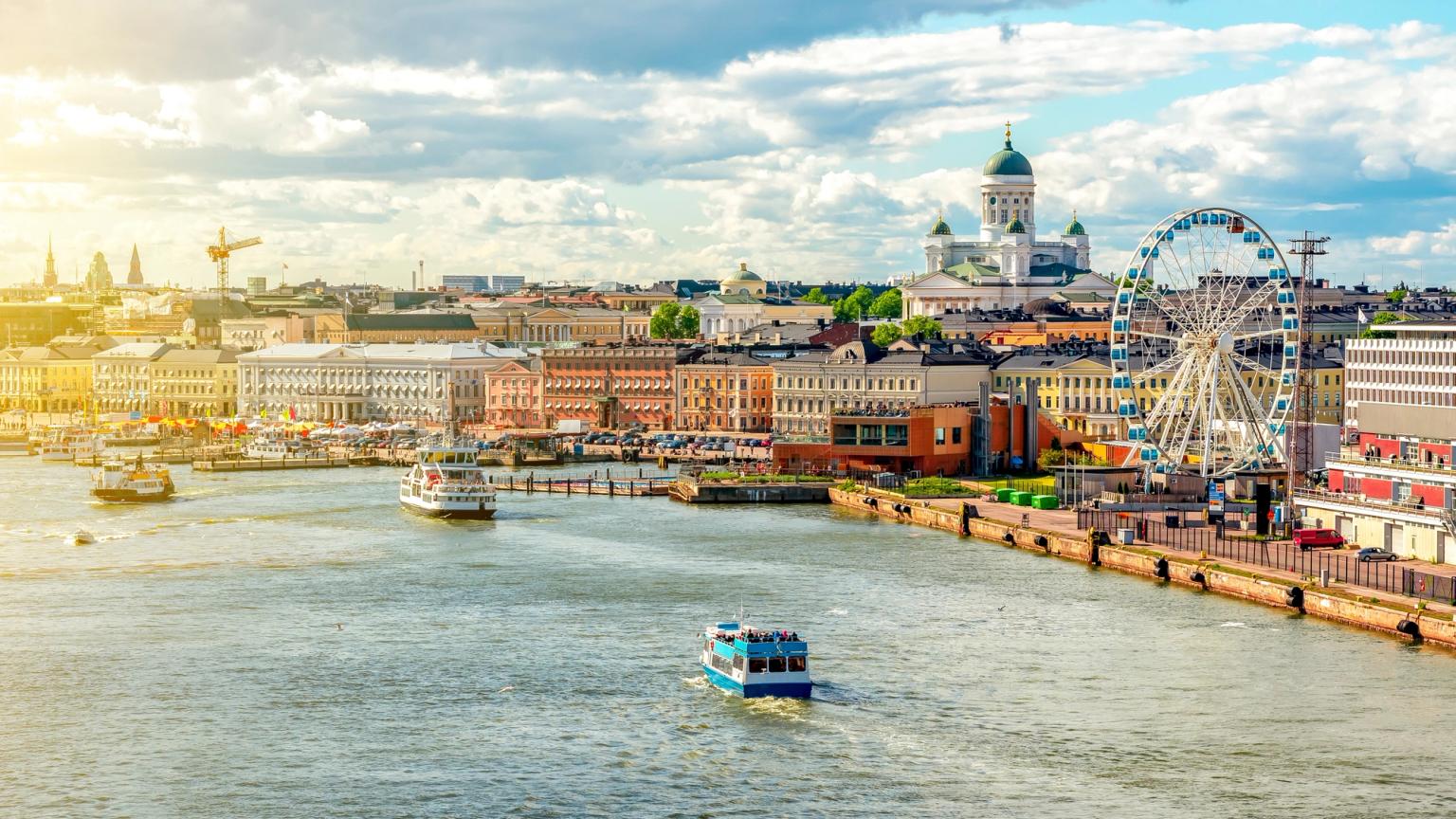 Helsinkis havneområde med båter, den hvite katedralen, et pariserhjul og fargerike bygninger under en solrik himmel.