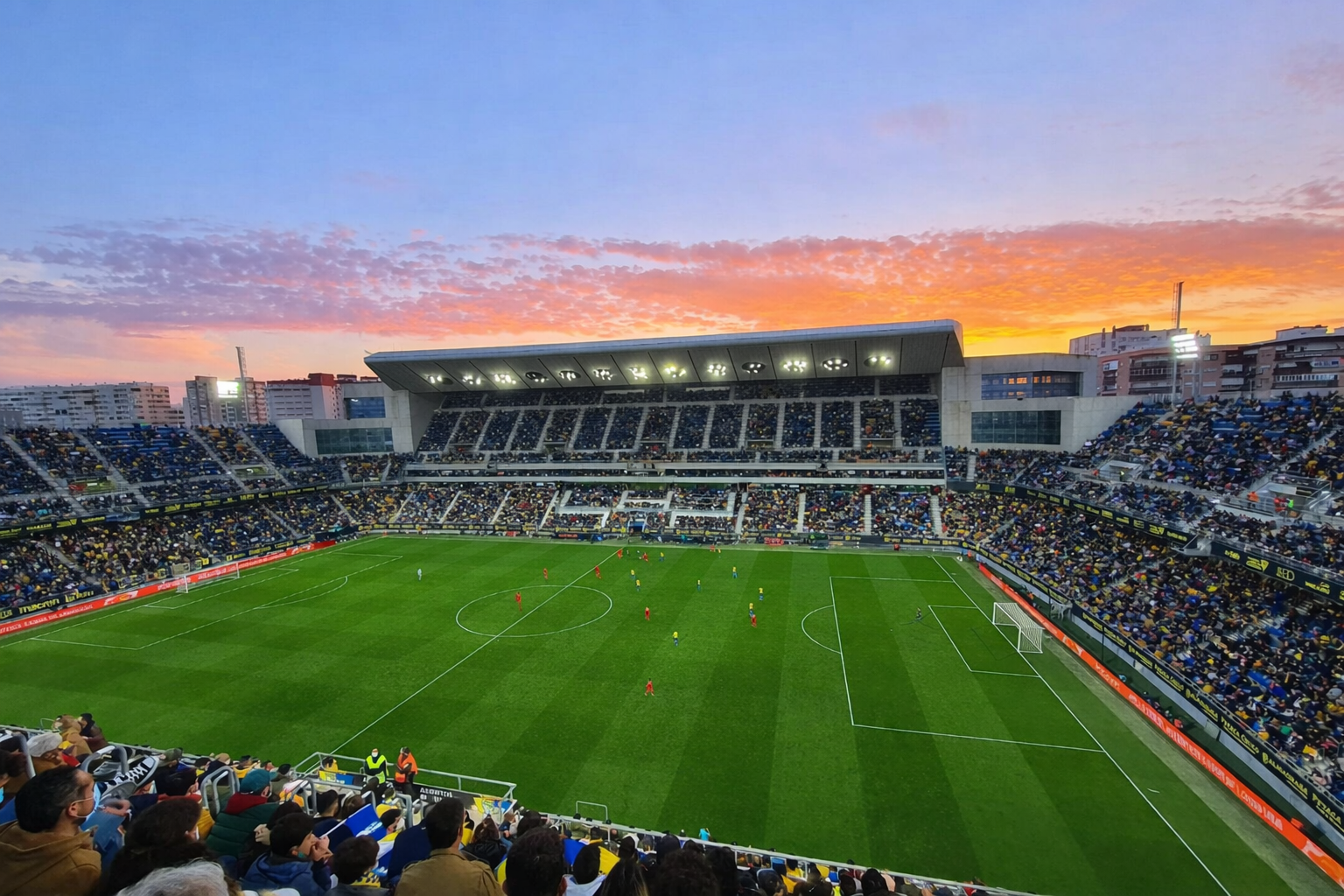 En livlig solnedgångshimmel över en fullsatt fotbollsstadion under en match.