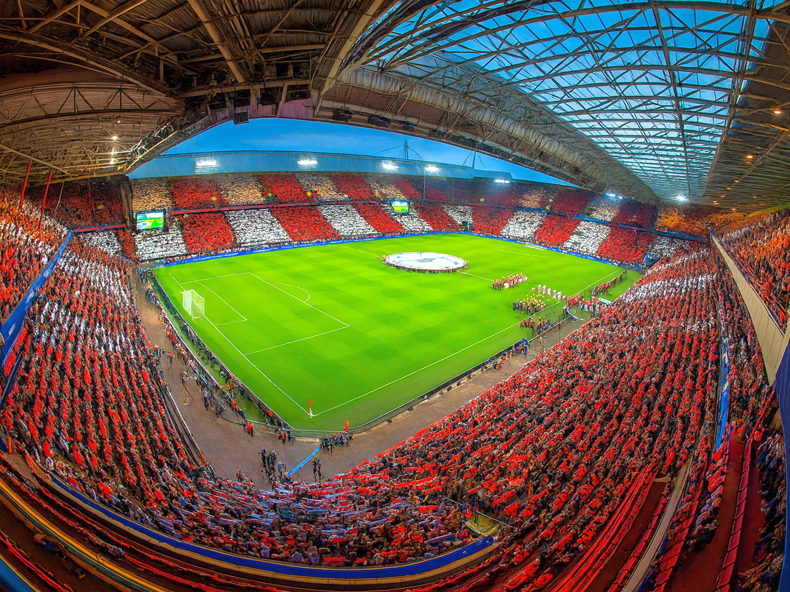 En vy ovanifrån av en fotbollsstadion full av fans som skapar röda och vita mönster på läktarna runt en grön plan.