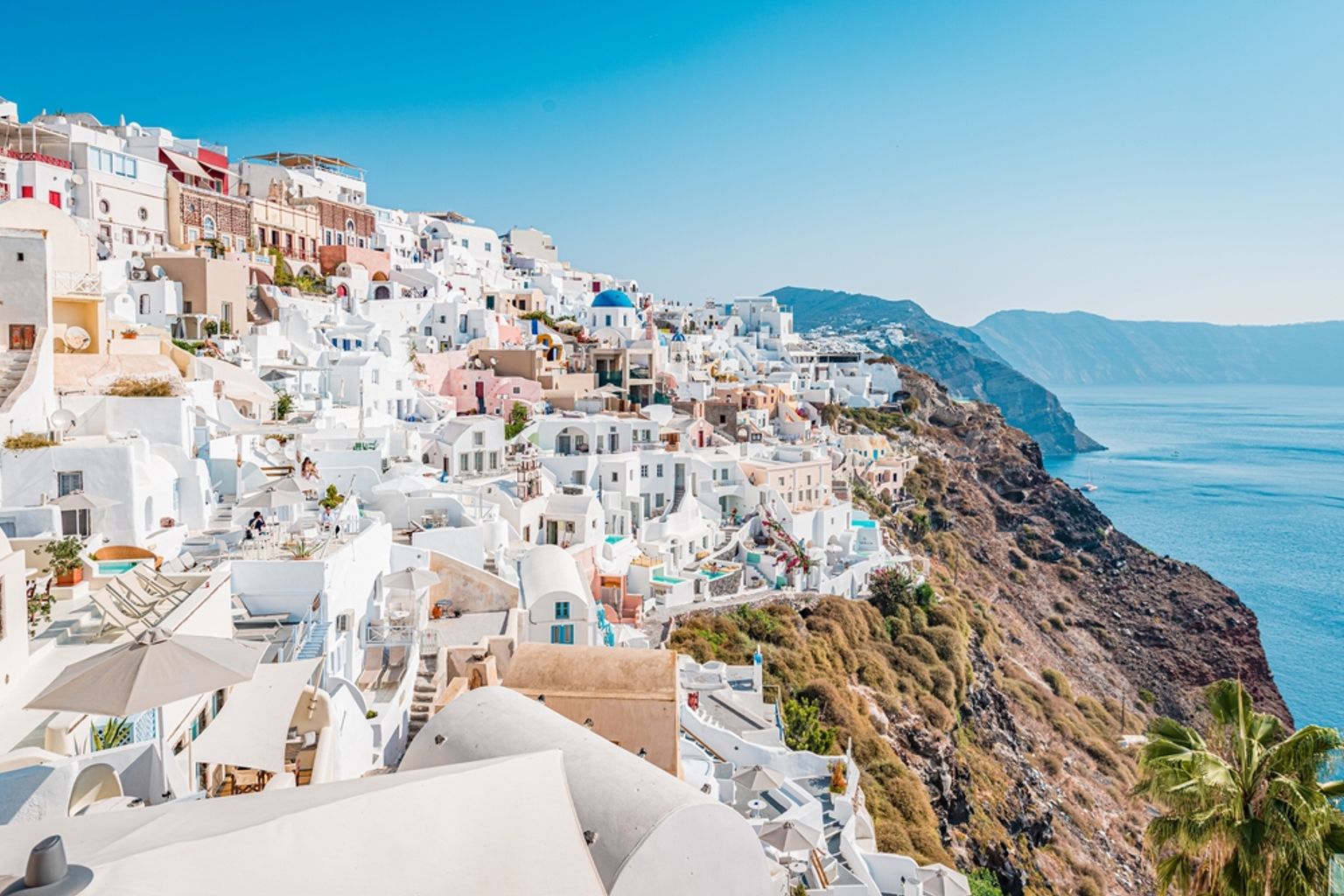Santorini klippeby med hvide bygninger og en blå kuppel med udsigt over det rolige blå hav.