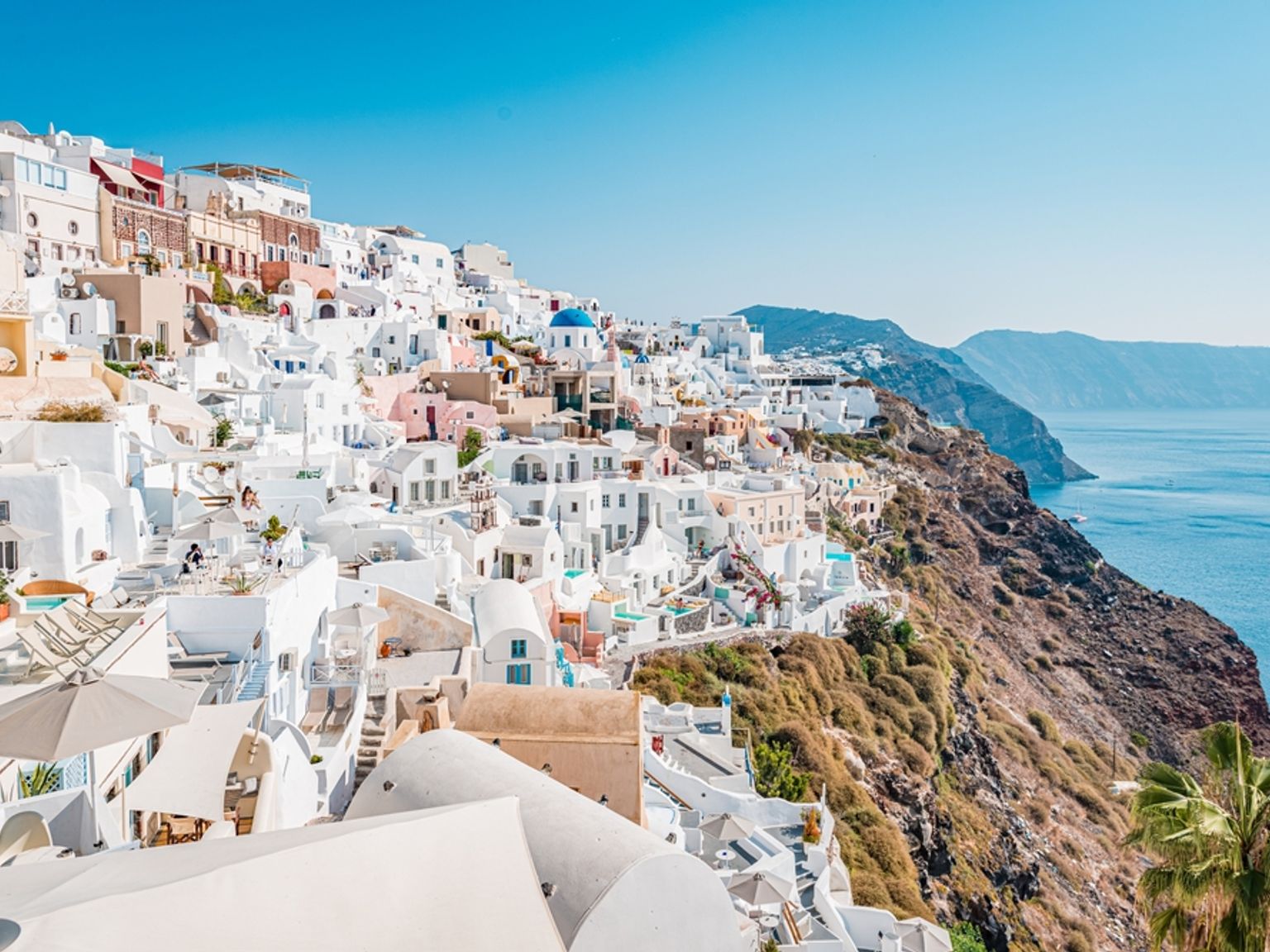 Santorini klippeby med hvite bygninger og en blå kuppel med utsikt over det rolige blå havet.