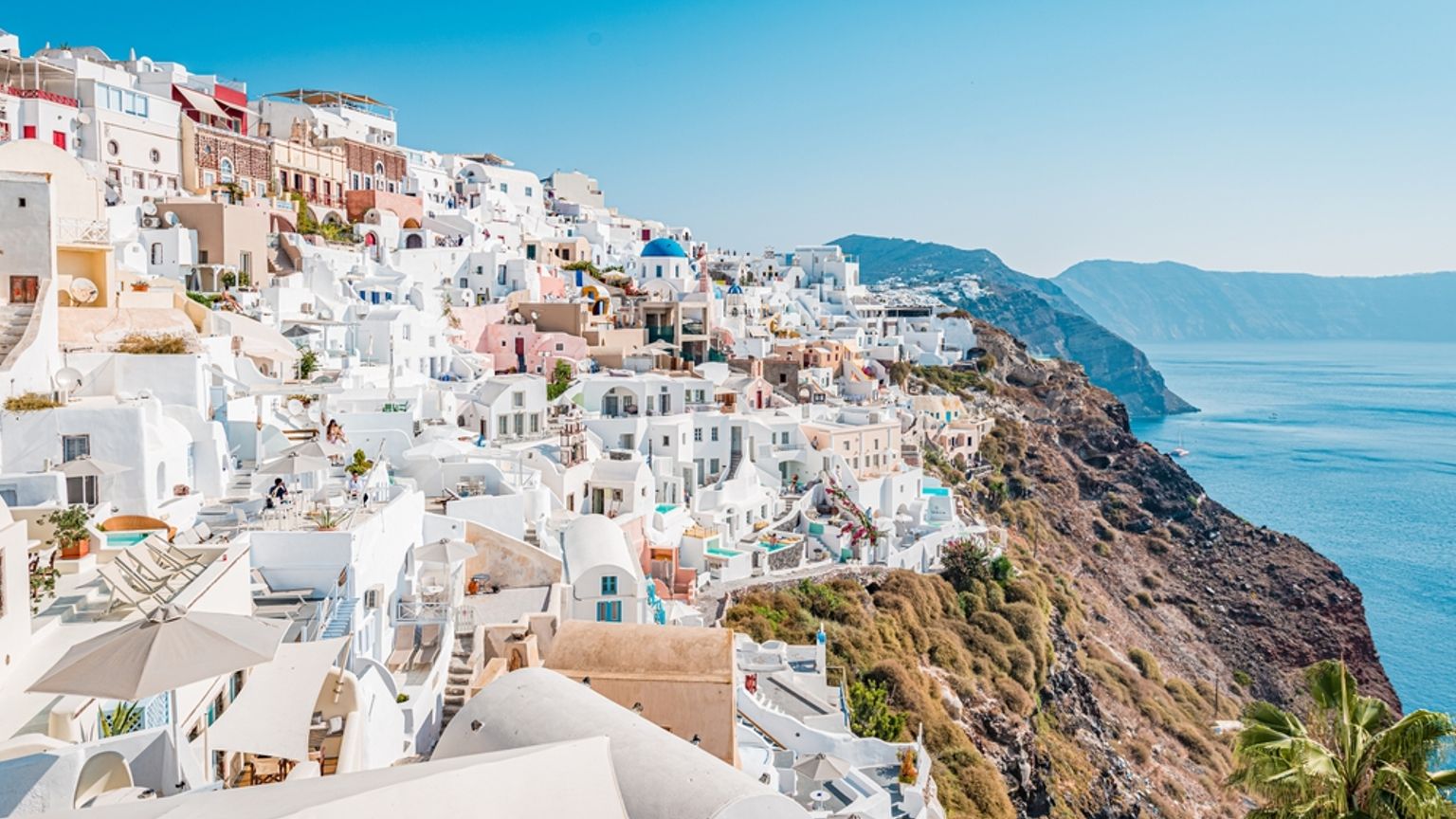 Santorini klippeby med hvide bygninger og en blå kuppel med udsigt over det rolige blå hav.