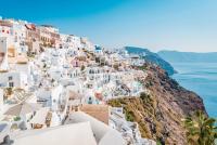 Santorini klippby med vita byggnader och en blå kupol med utsikt över det lugna blå havet.