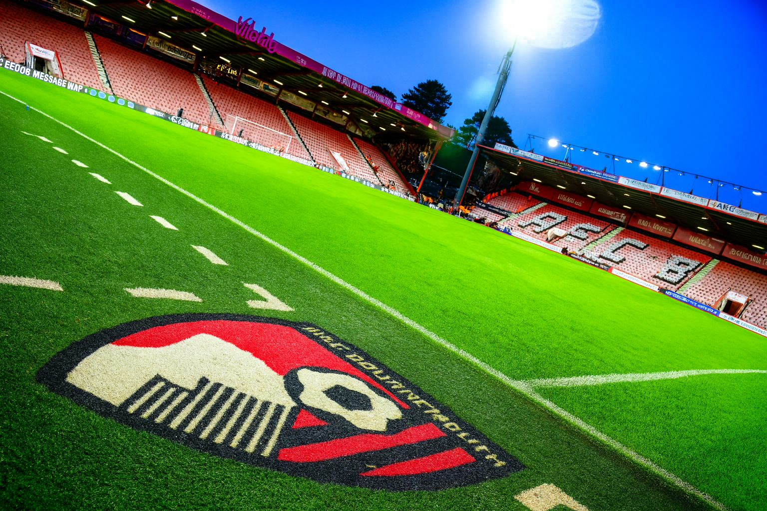 Fußballplatz mit AFC Bournemouth-Logo, roten Stadionsitzen und hellem Flutlicht.