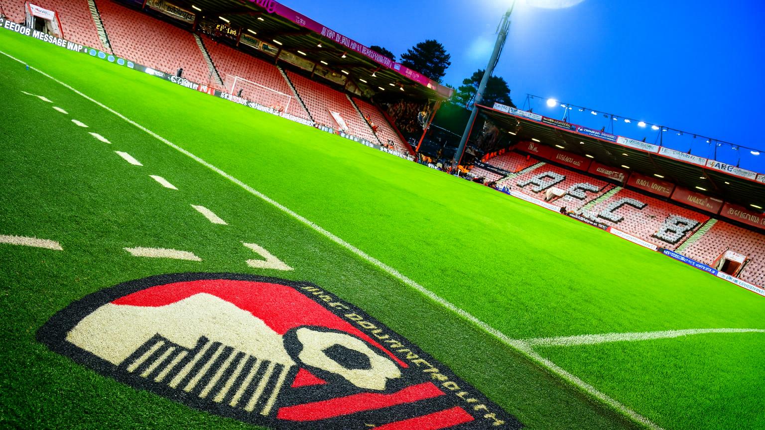 Football pitch with AFC Bournemouth logo, red stadium seats, and bright floodlight.