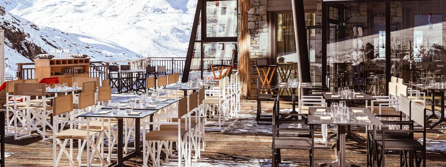 det er mange bord og stoler utenfor en restaurant med fjell i bakgrunnen, Altapura Hôtel & Spa Val Thorens.