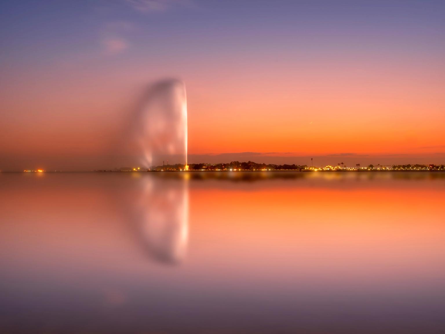 en fontene reflekteres i vannet ved solnedgang