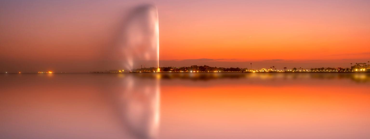en fontän reflekteras i vattnet vid solnedgången