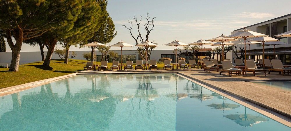 En stor utomhuspool med solstolar, parasoller och en modern byggnad i bakgrunden. Octant Evora