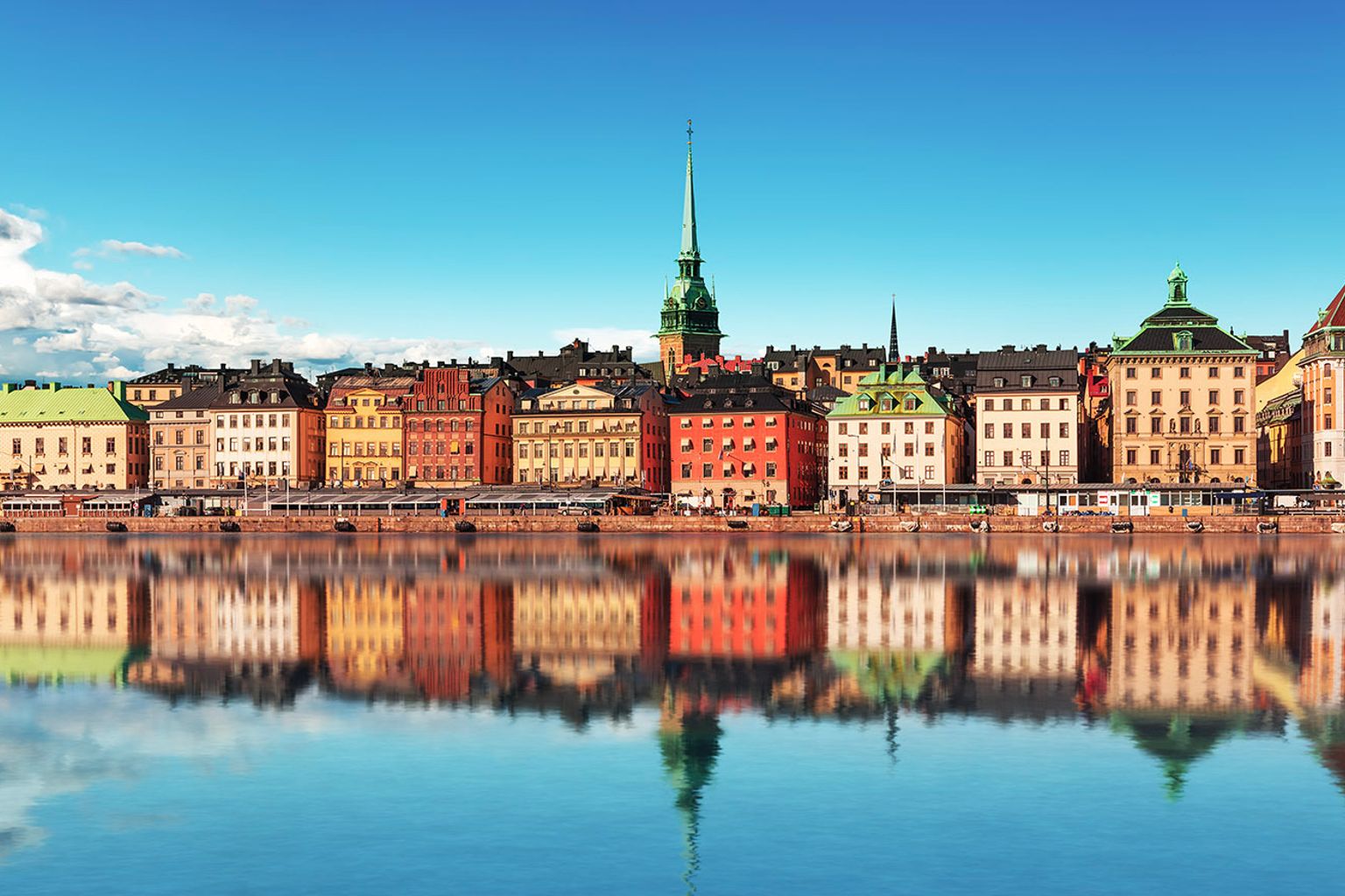 a row of colorful buildings are reflected in a body of water.