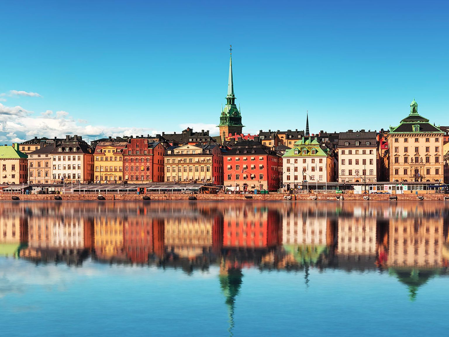 en rekke fargerike bygninger reflekteres i et vann.