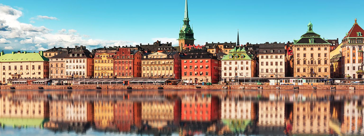 en række farverige bygninger reflekteres i et vandområde.