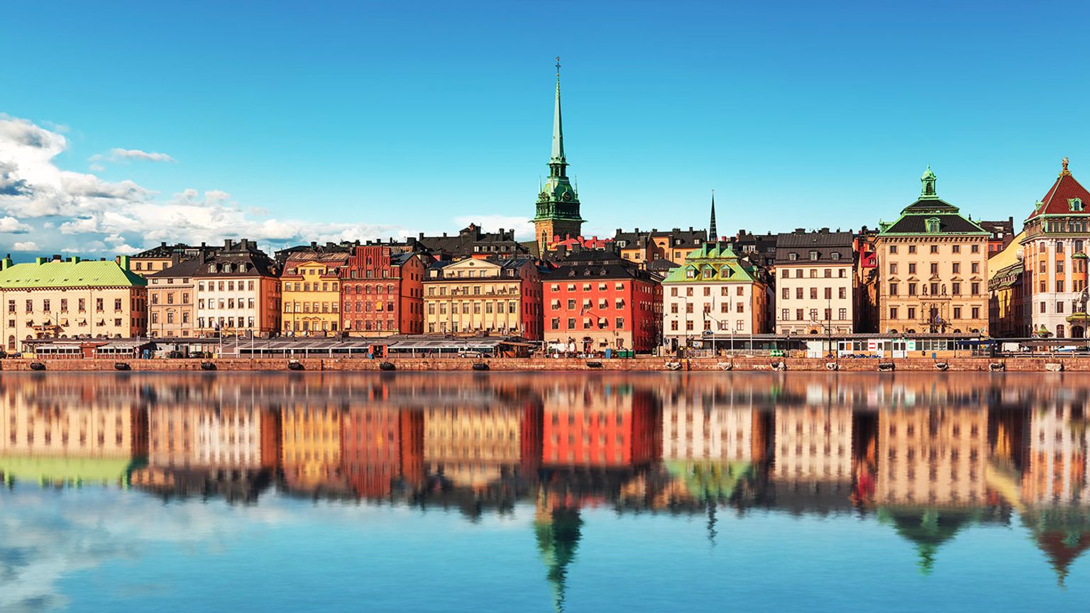 en række farverige bygninger reflekteres i et vandområde.