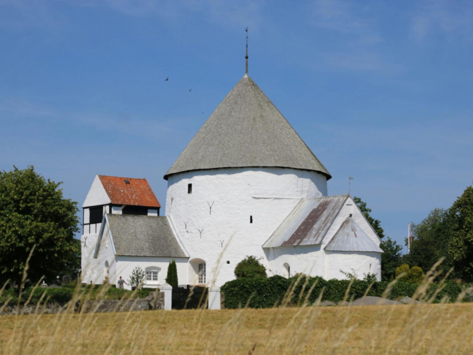 en vit kyrka med ett koniskt tak står mitt på en äng.