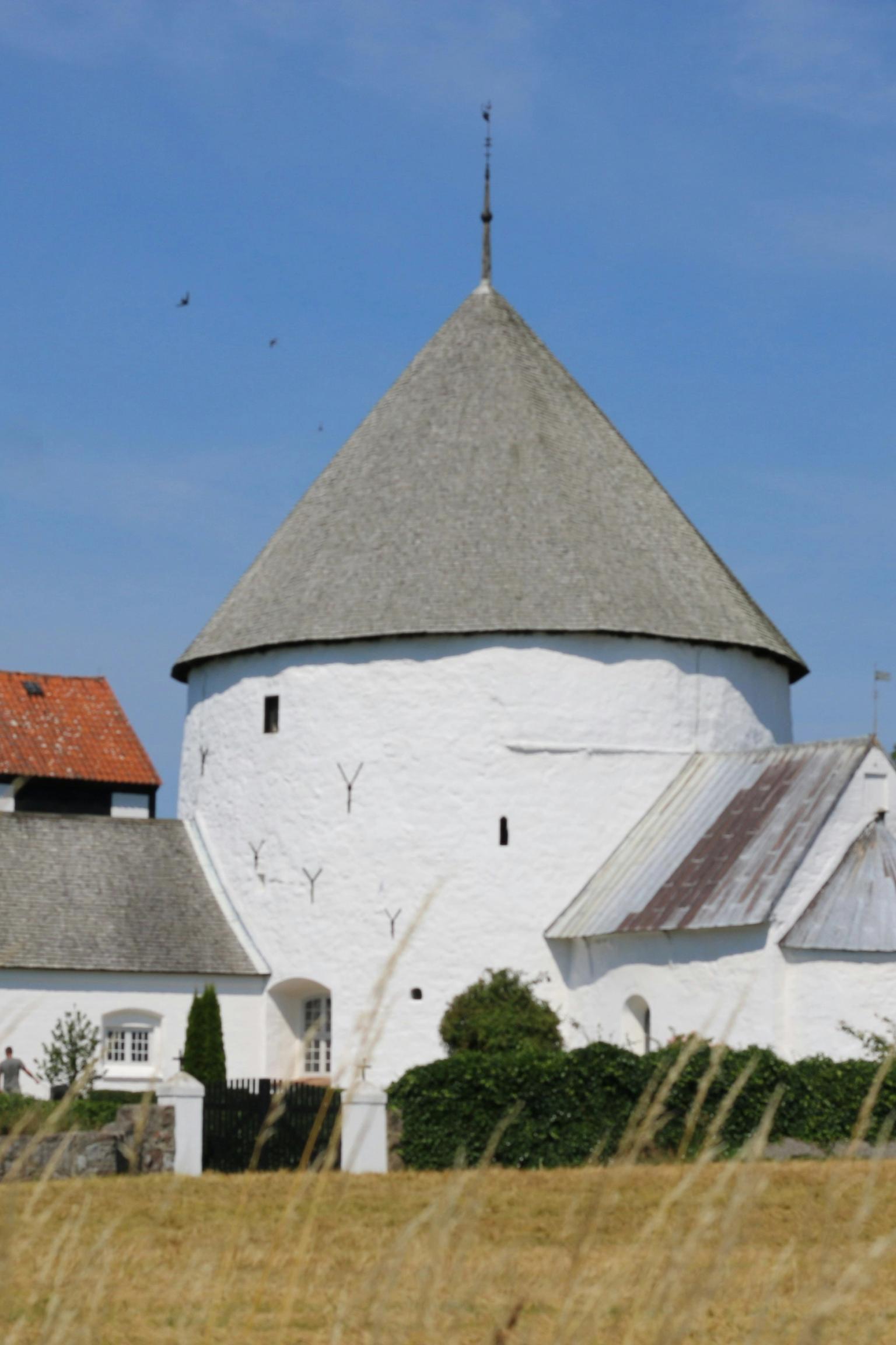 en vit kyrka med ett koniskt tak står mitt på en äng.