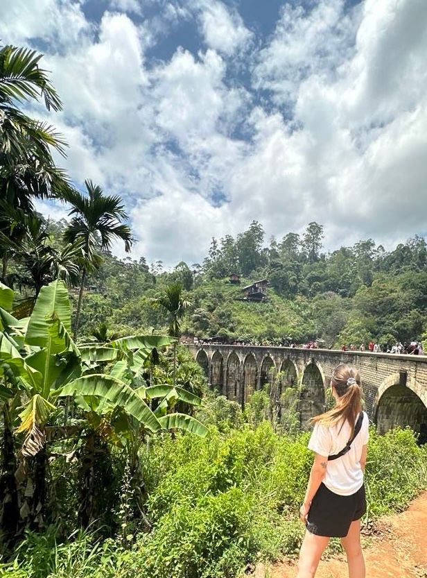 eine Frau steht vor einer Brücke im Dschungel.