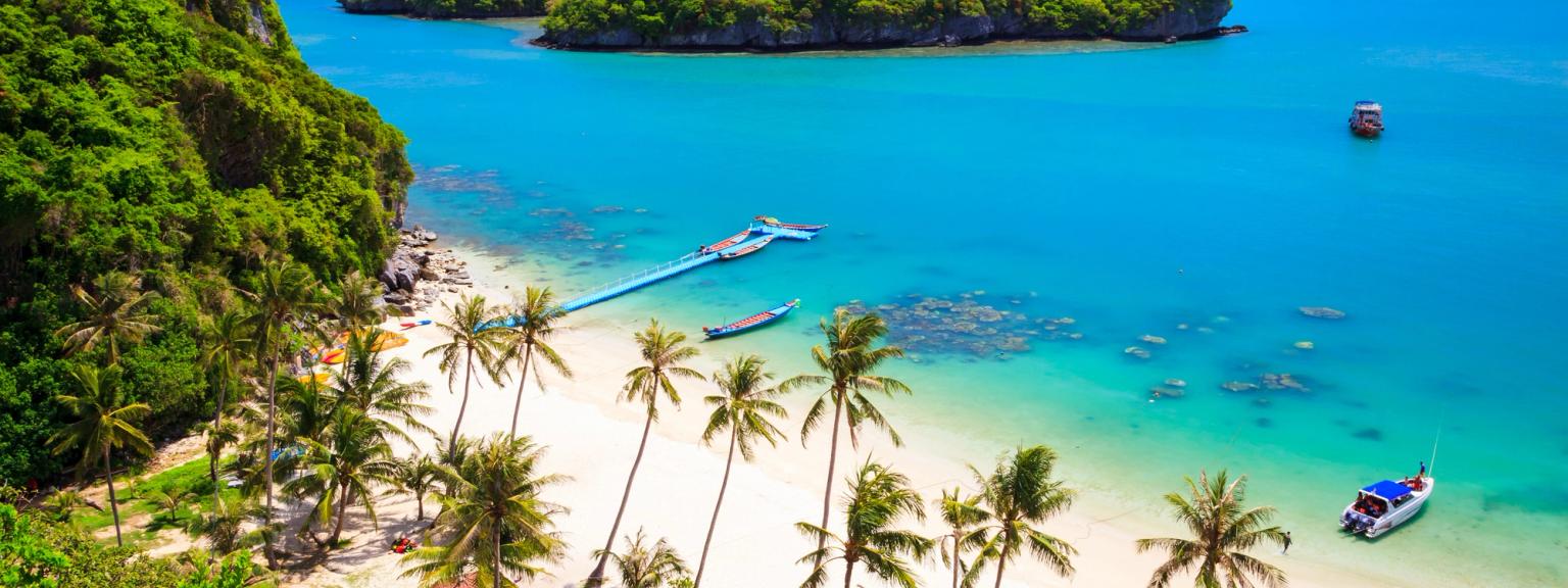 en flygvy av en tropisk strand med palmer och en båt i vattnet på Koh Samui.