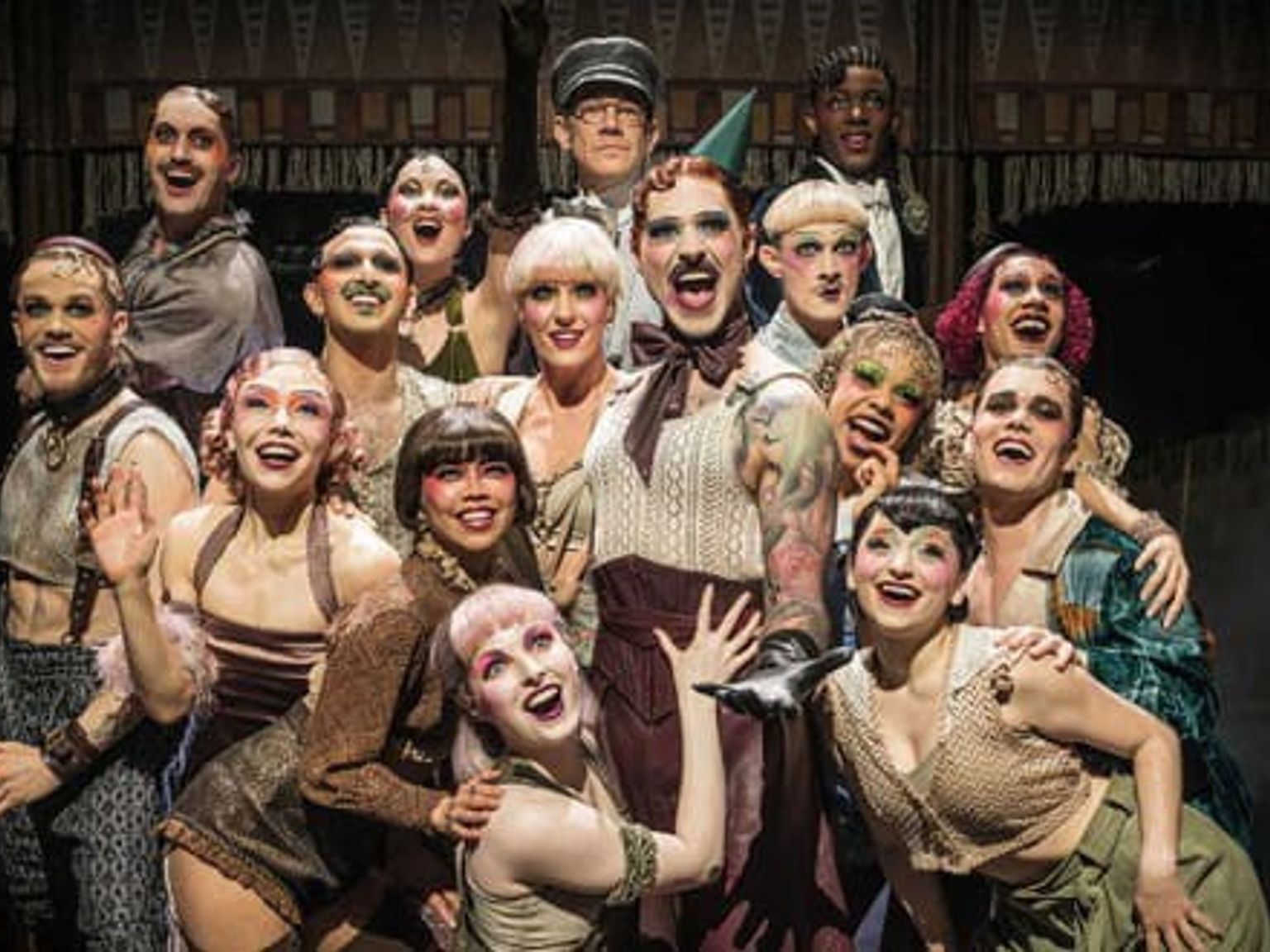 Duży, uśmiechnięty zespół wykonawców w teatralnych kostiumach i z dramatycznym makijażem.