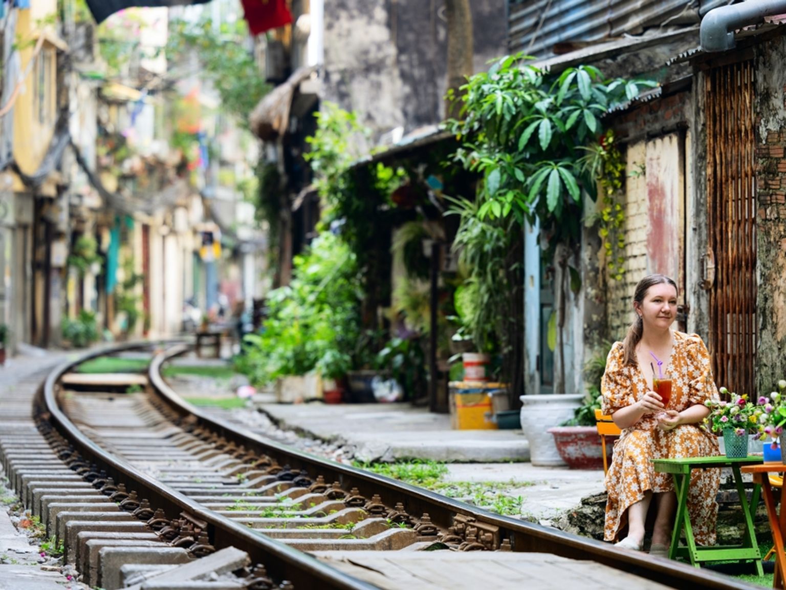 En kvinde sidder ved et bord ved siden af jernbanespor, der buer gennem en smal bygade omgivet af gamle bygninger. Hanoi, Vietnam