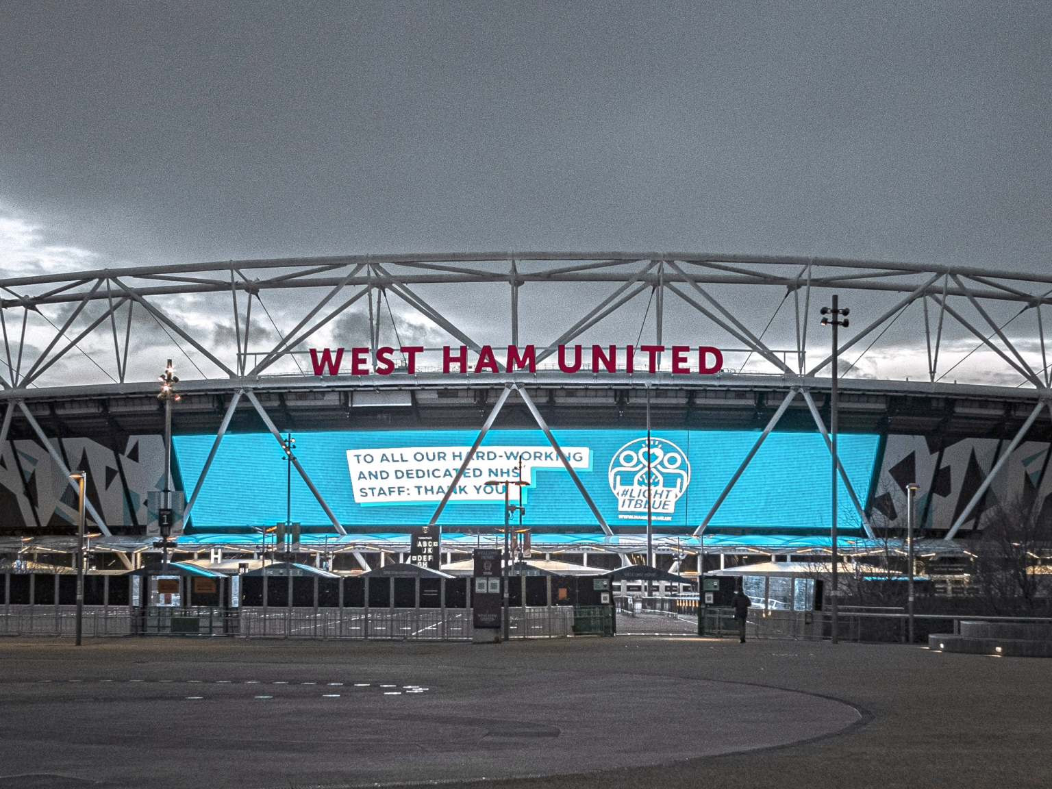 West Ham United stadion under en skyet himmel, med en stor blå skærm, der viser "TIL ALLE VORES HÅRDTARBEJDENDE OG DEDIKEREDE NHS-PERSONALE: TAK."