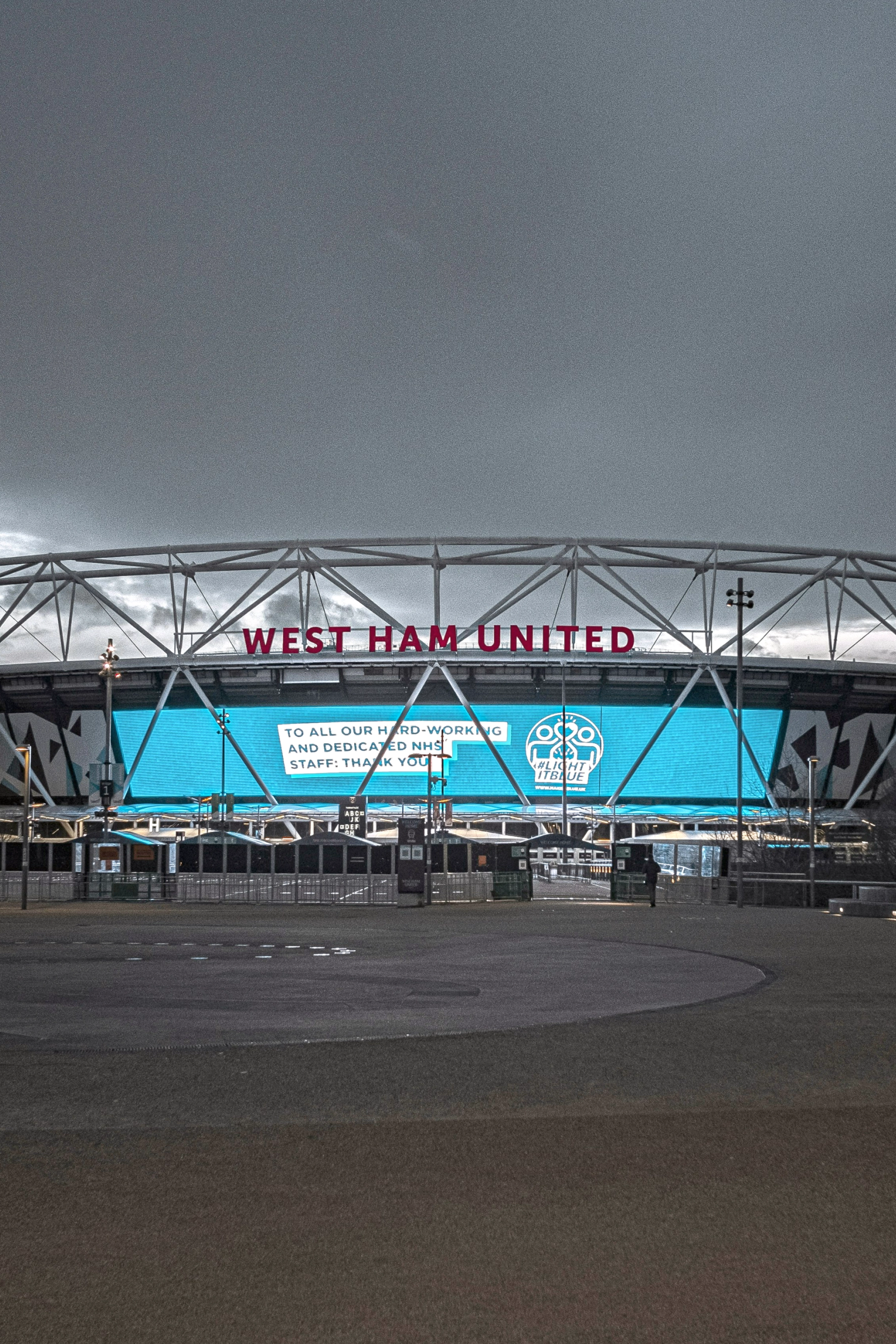 West Ham United stadion under en skyet himmel, med en stor blå skærm, der viser "TIL ALLE VORES HÅRDTARBEJDENDE OG DEDIKEREDE NHS-PERSONALE: TAK."