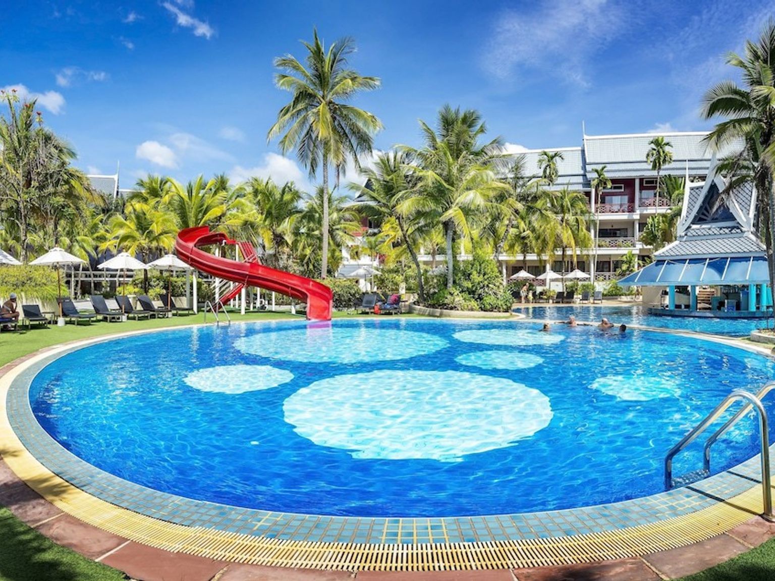 et stort svømmebasseng med en rød sklie i midten av det omgitt av palmetrær