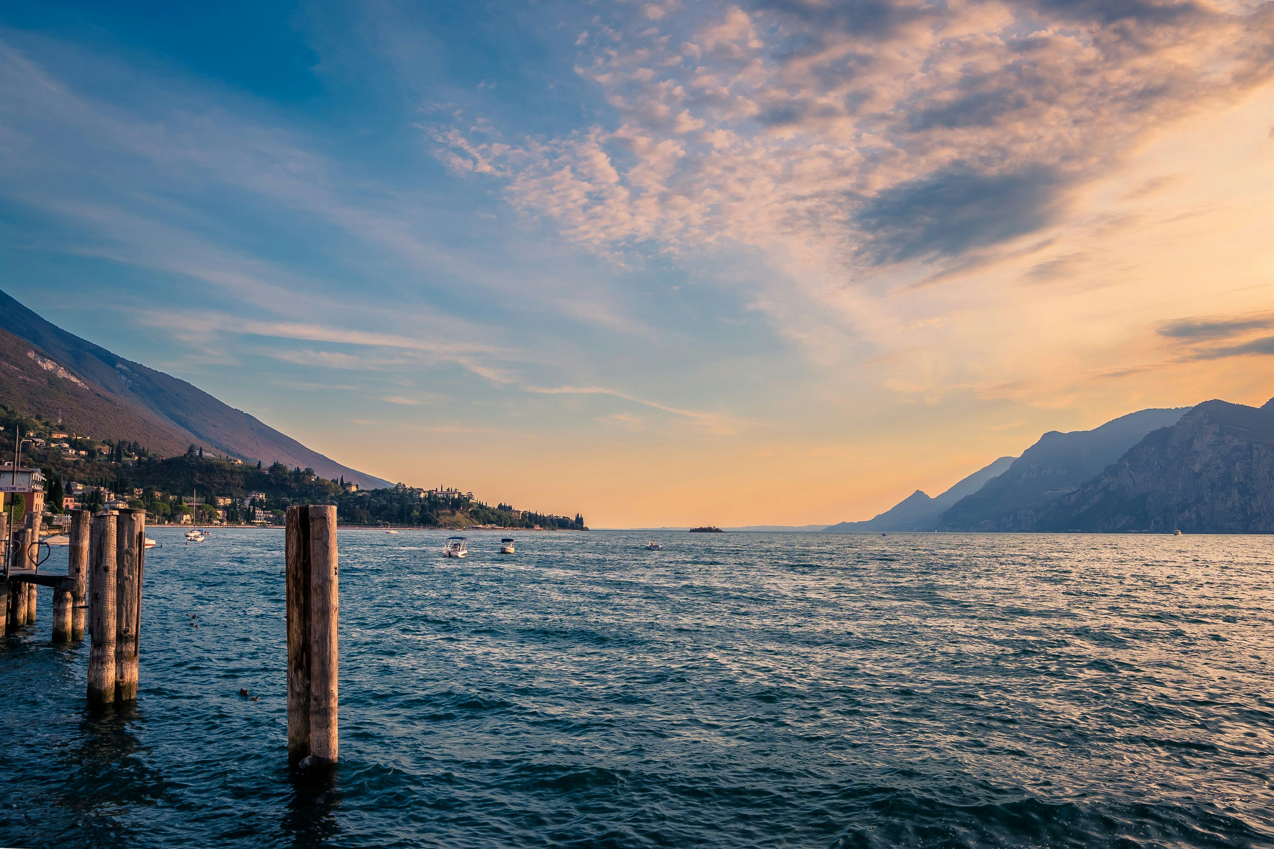 Naturskjønn innsjø med fjell, båter og trebryggestolper ved solnedgang. Gardasjøen, Italia