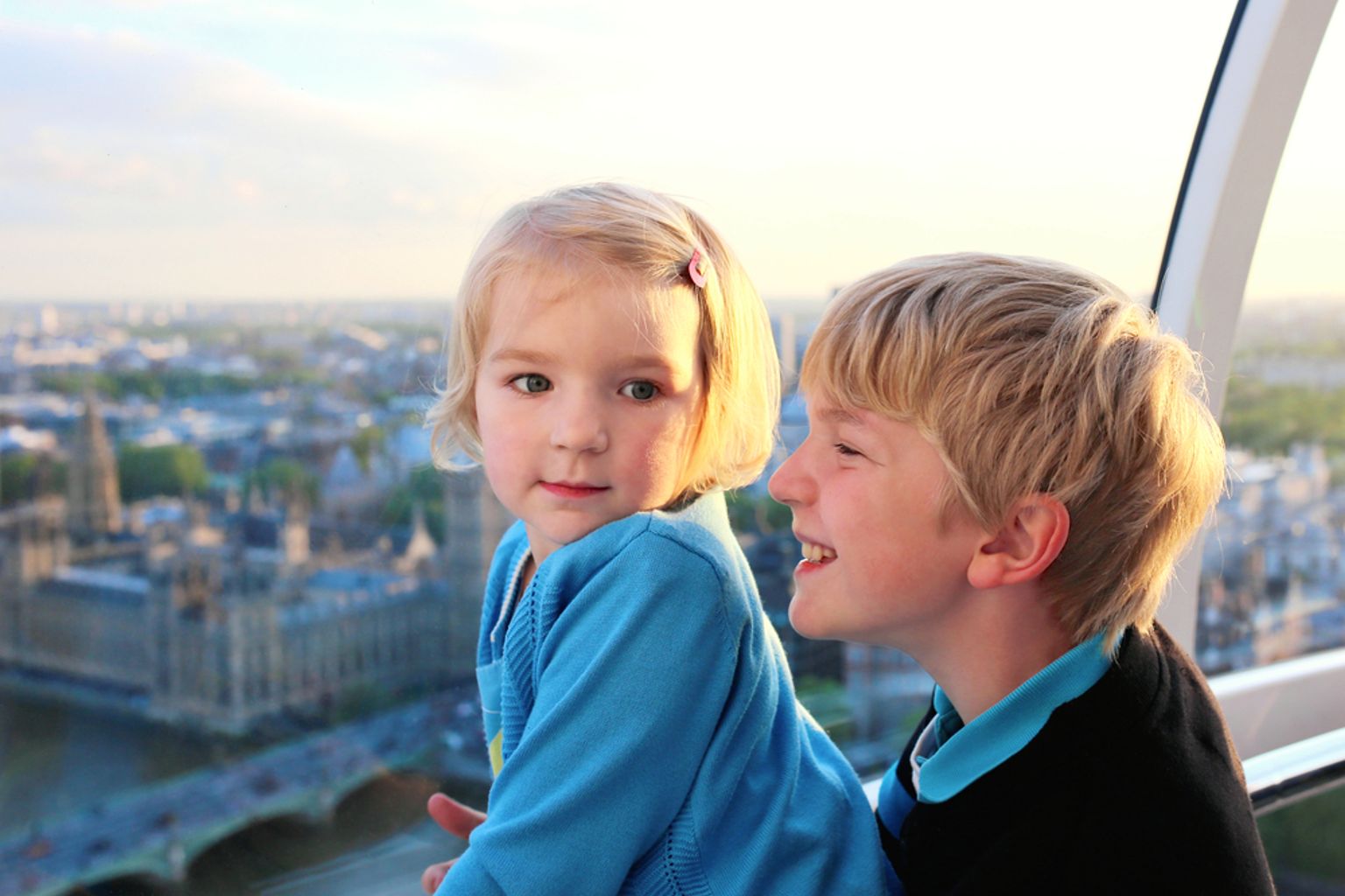 To barn i en gondol på et pariserhjul med utsikt over Londons bysilhuett og parlamentsbygningen.