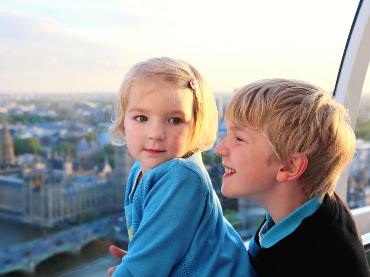 To barn i en gondol på et pariserhjul med utsikt over Londons bysilhuett og parlamentsbygningen.
