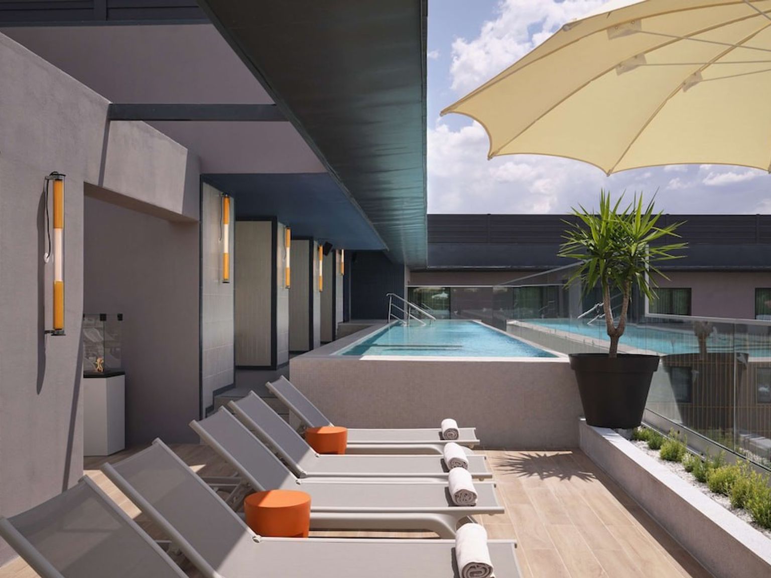 Modern takterrass med en swimmingpool, solstolar, ett parasoll och krukväxter.