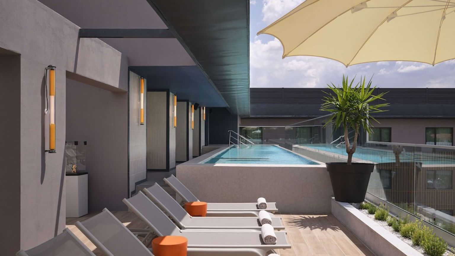 Modern takterrass med en swimmingpool, solstolar, ett parasoll och krukväxter.