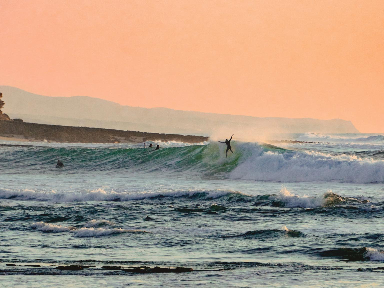 a surfer rides a wave in the ocean at sunset