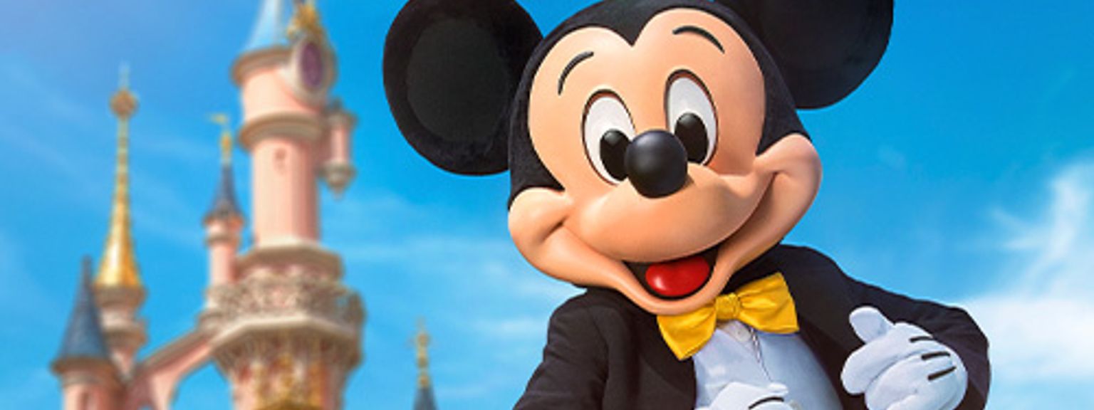 mickey mouse is standing in front of a castle.