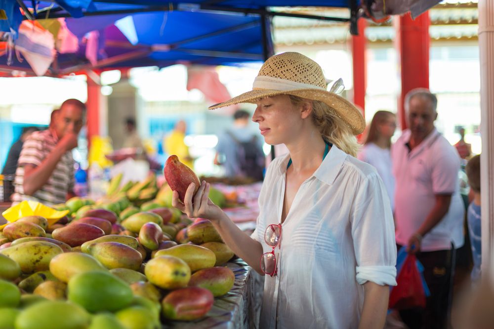 Kvinna i stråhatt som undersöker en mango på en fruktmarknad. Seychellerna