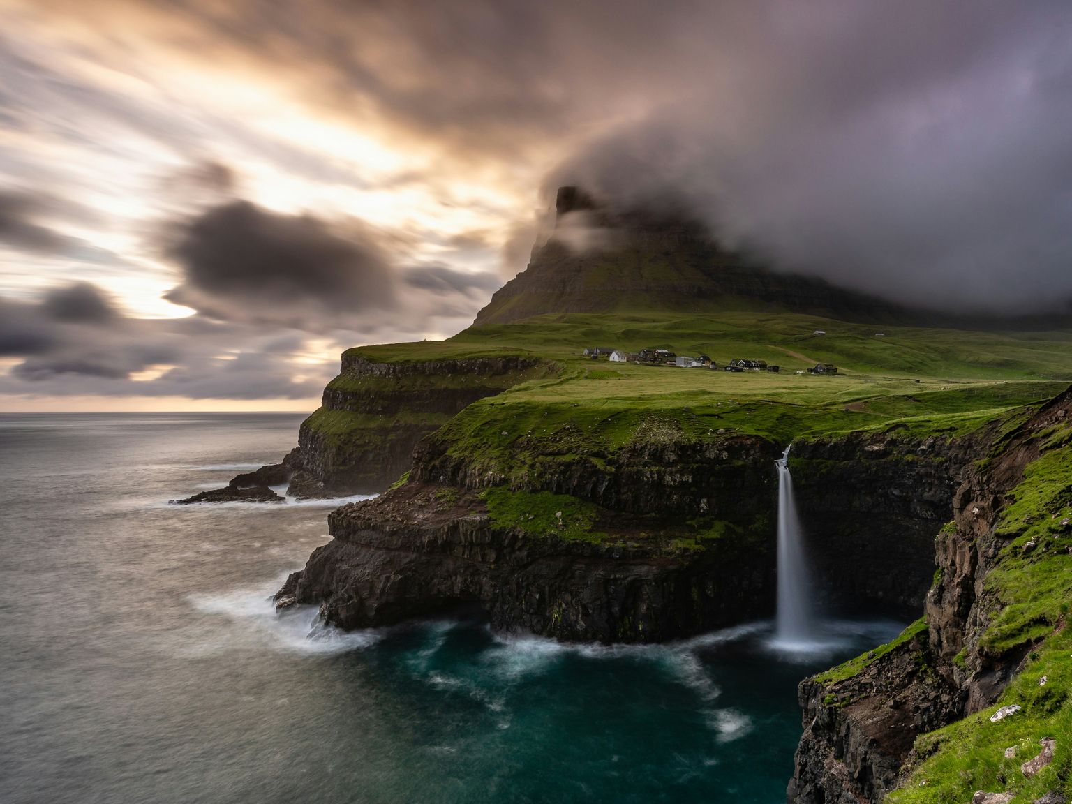 a waterfall on a cliff overlooking the ocean with a mountain in the background