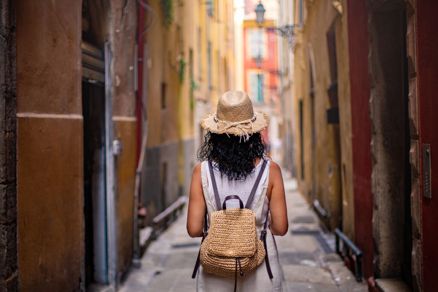 En person med stråhatt och ryggsäck går nerför en smal, färgglad gränd. Nice, Frankrike