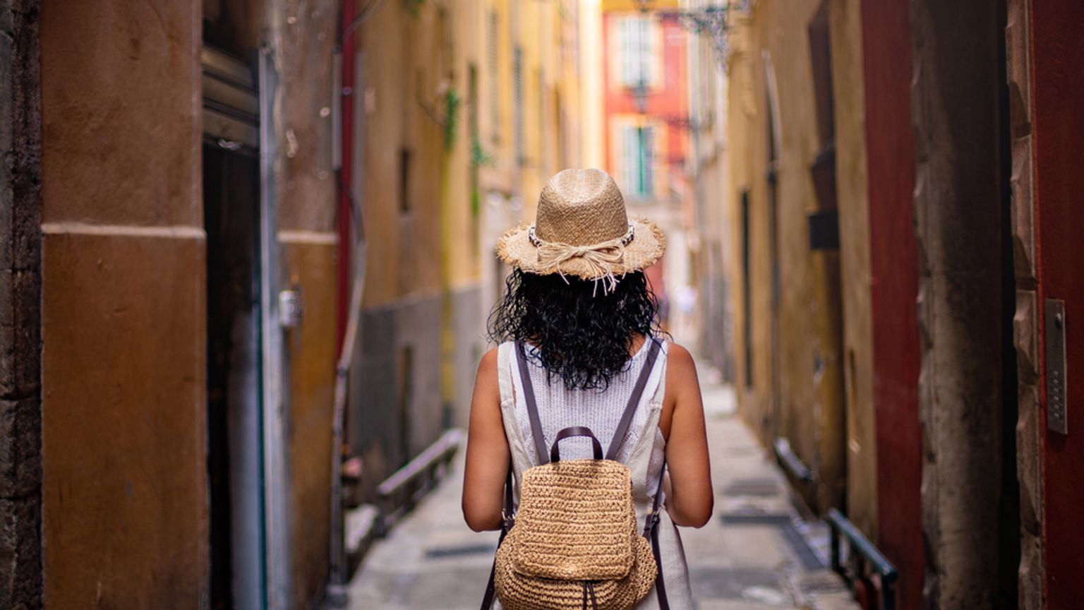 En person med stråhatt och ryggsäck går nerför en smal, färgglad gränd. Nice, Frankrike
