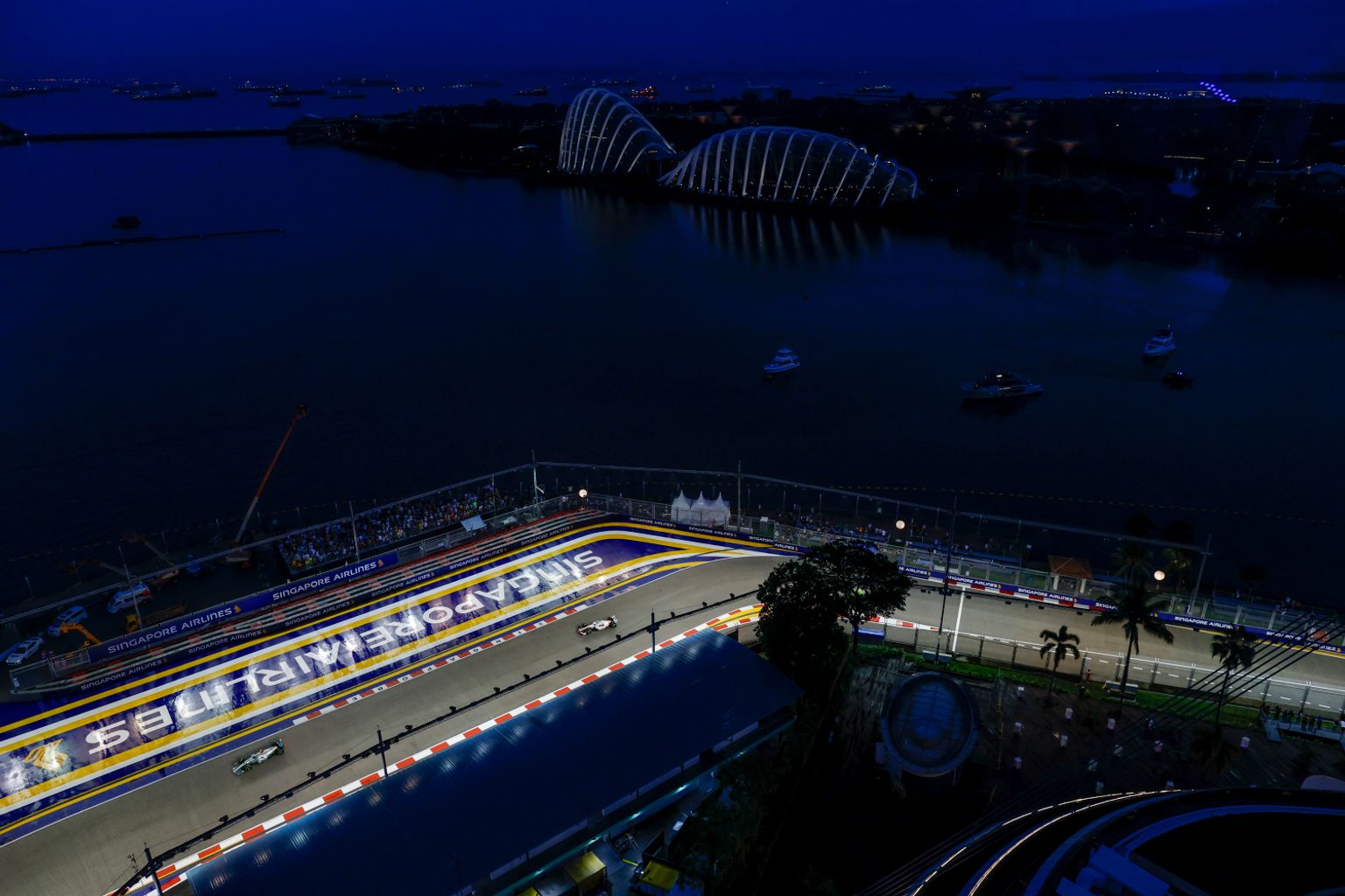 Luftfoto om natten av Singapore F1-banen med racerbiler, opplyste Gardens by the Bay og båter i bukten.
