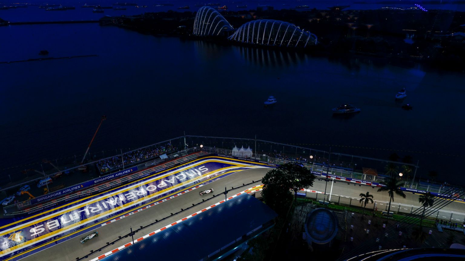 Luftfoto om natten av Singapore F1-banen med racerbiler, opplyste Gardens by the Bay og båter i bukten.