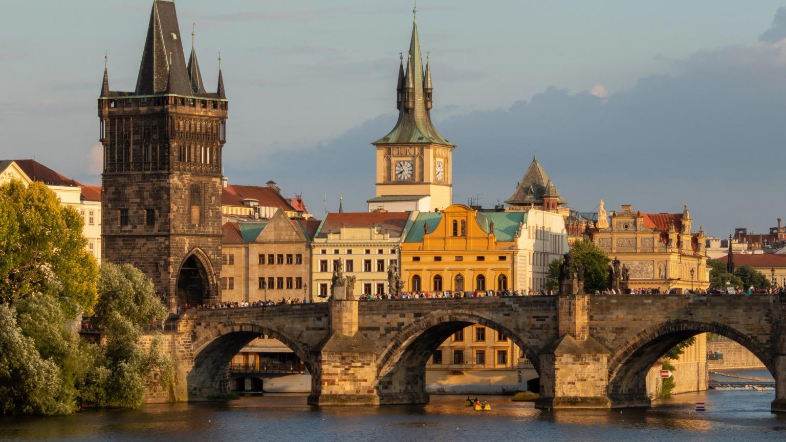 en bro över en flod med ett klocktorn i bakgrunden. Prag