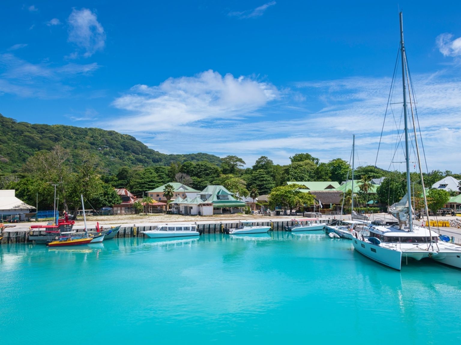 En levende turkis havn med både, en landsby og frodige bakker under en blå himmel. Seychellerne