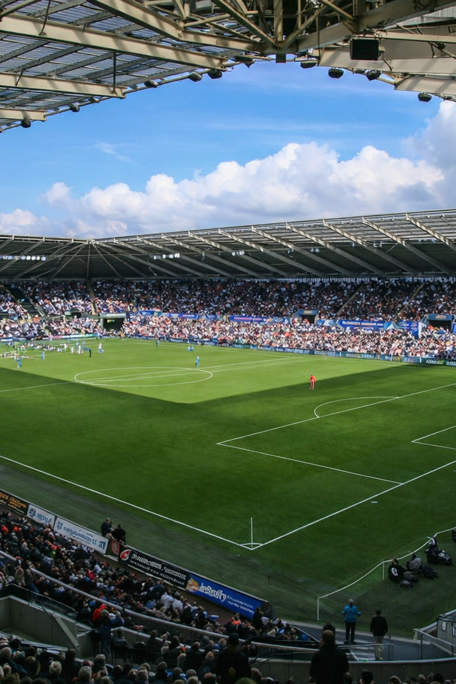 A large, packed football stadium during a match, with a clear blue sky overhead.