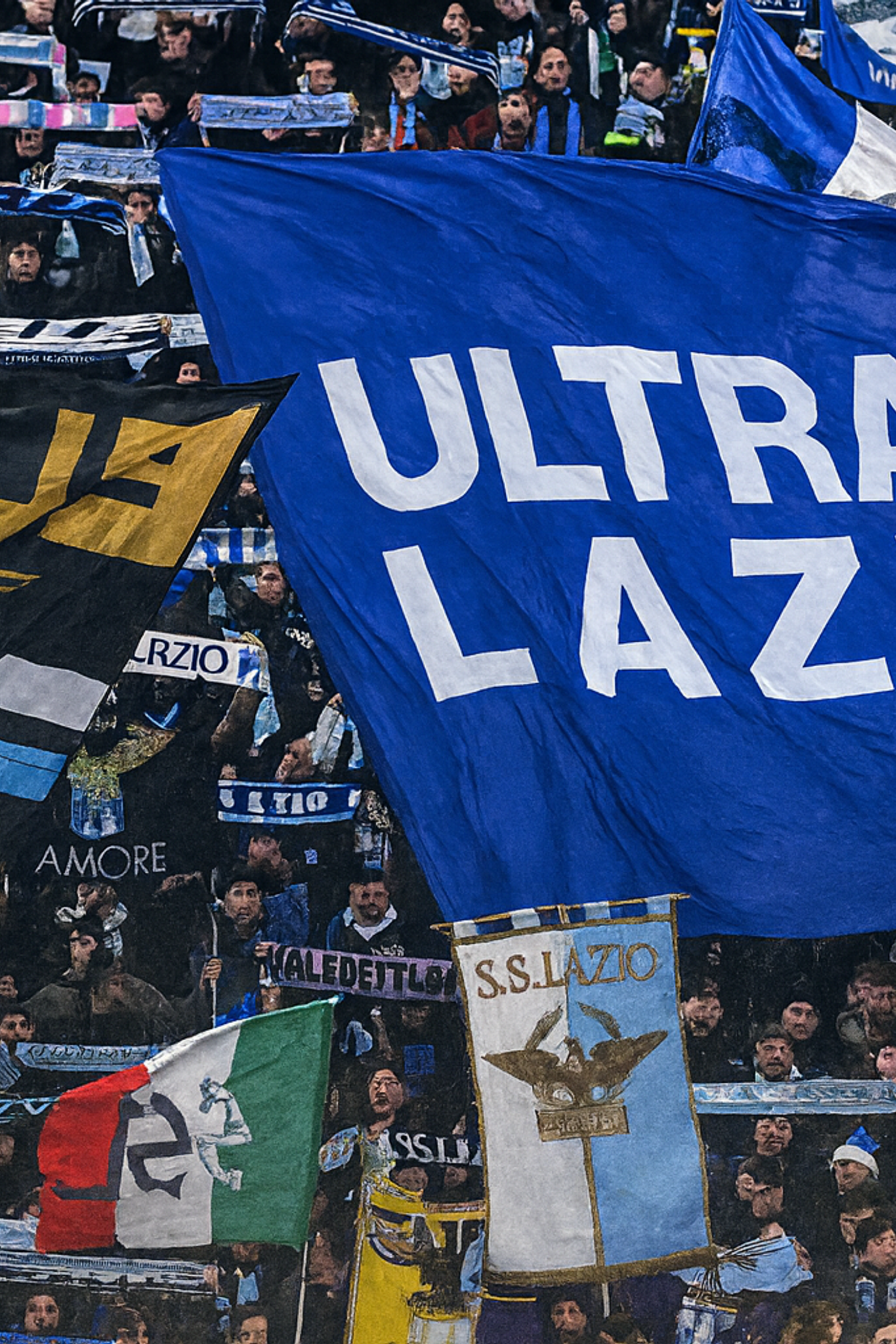 Lazio fotbollsfans håller stora flaggor, inklusive en blå med "ULTRAS LAZIO" skrivet i vitt.