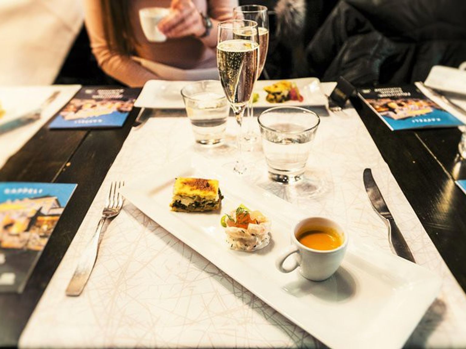 a table with plates of food, glasses of wine, and a cup of soup