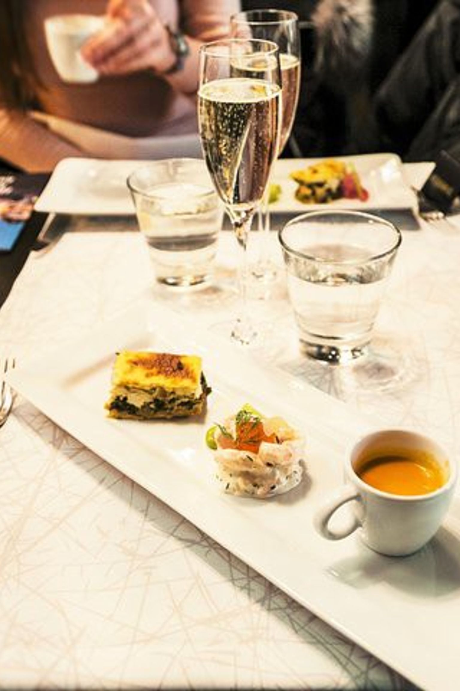 a table with plates of food, glasses of wine, and a cup of soup