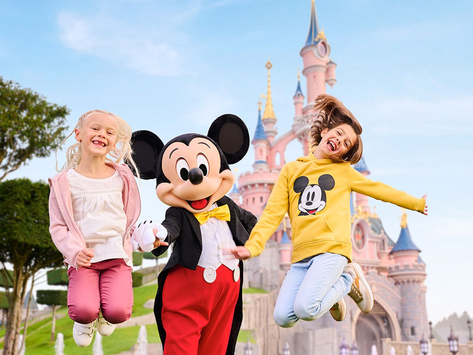 två barn hoppar i luften med mickey mouse framför ett slott