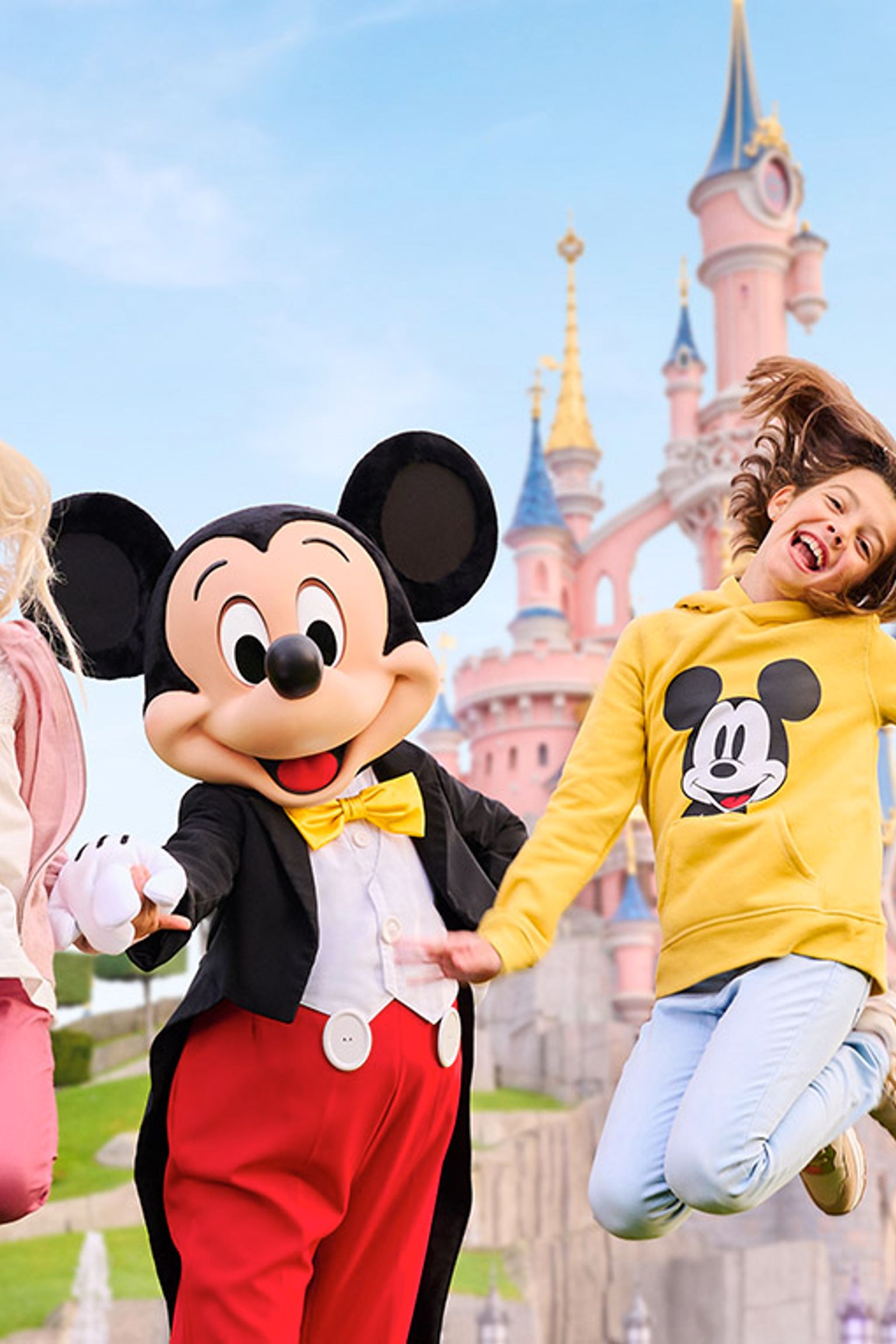 två barn hoppar i luften med mickey mouse framför ett slott
