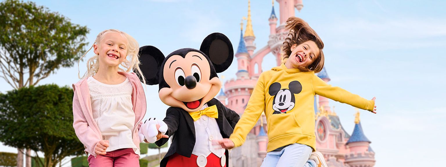 två barn hoppar i luften med mickey mouse framför ett slott