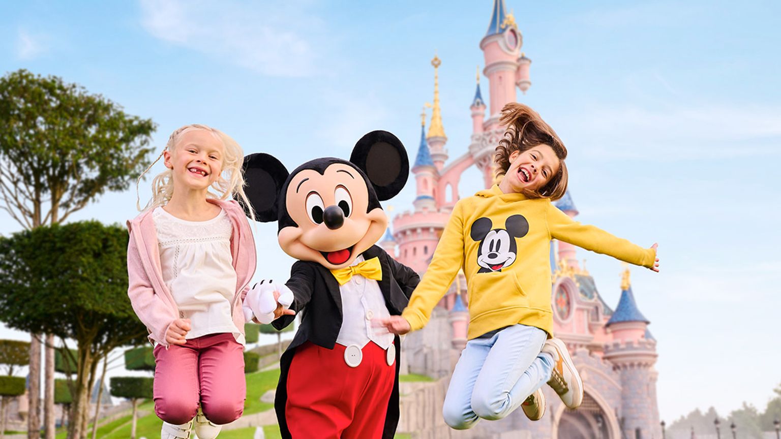 två barn hoppar i luften med mickey mouse framför ett slott