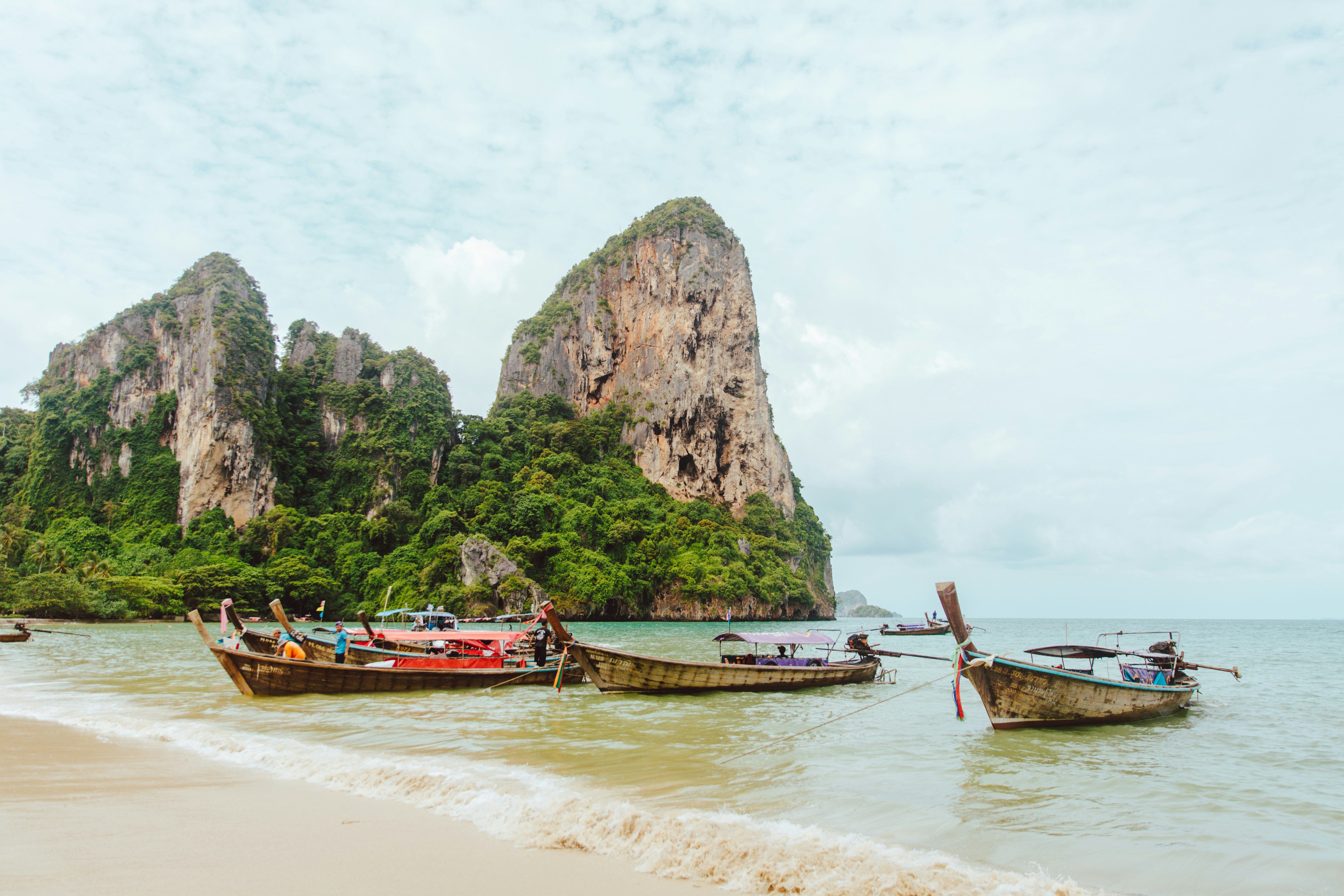 en gruppe båter er fortøyd på Railay Beach i Thailand med et fjell i bakgrunnen